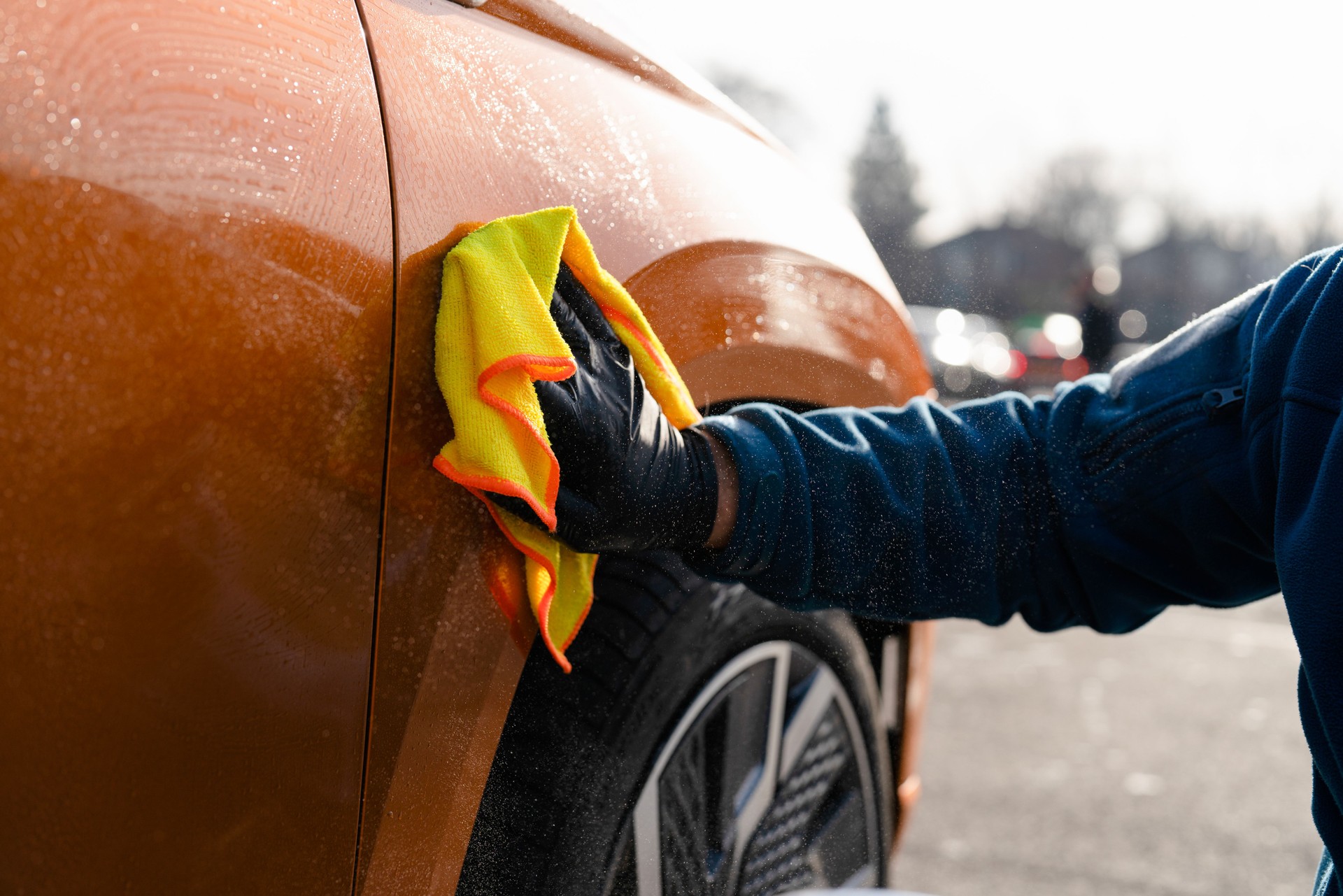 Car detailing session taking place on a sunny day with a focus on polishing the surface using a microfiber cloth in an outdoor setting
